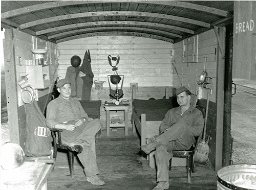 Inside the box car that is set up as a living-quarter with two soldiers sitting in chairs.